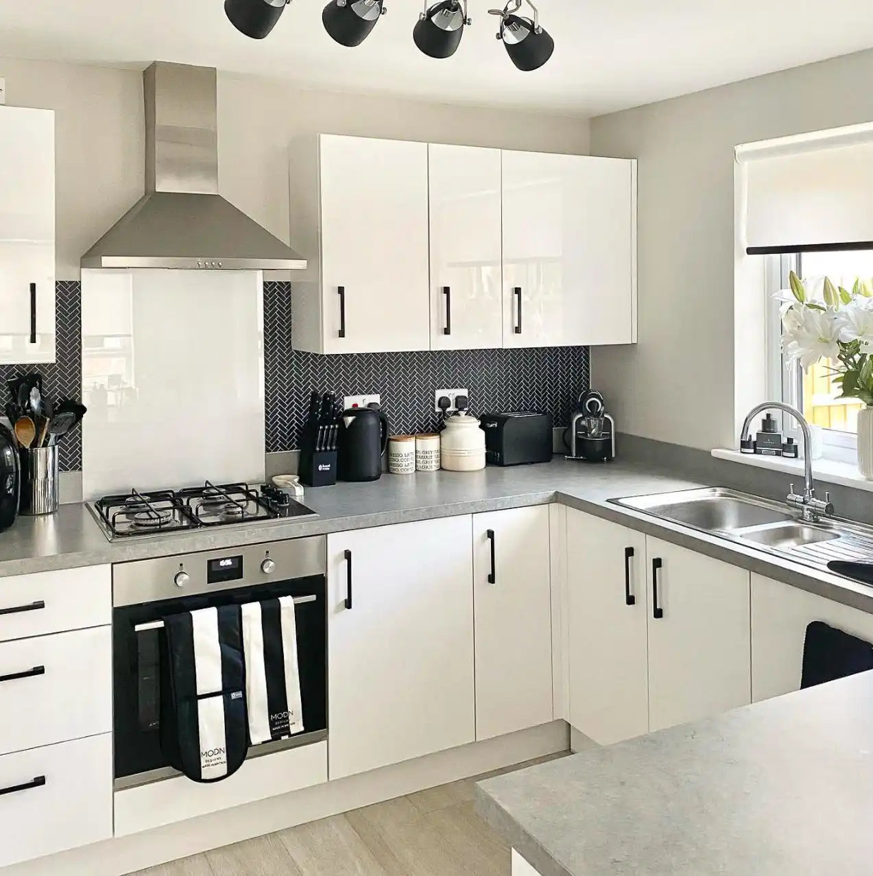 Modern L-shaped kitchen with white cabinets and black backsplash.